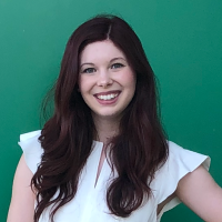 headshot of a smiling woman with brown hair standing in front of a teal background