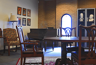 room with tables, chairs, lamp, piano and pictures hung on the wall